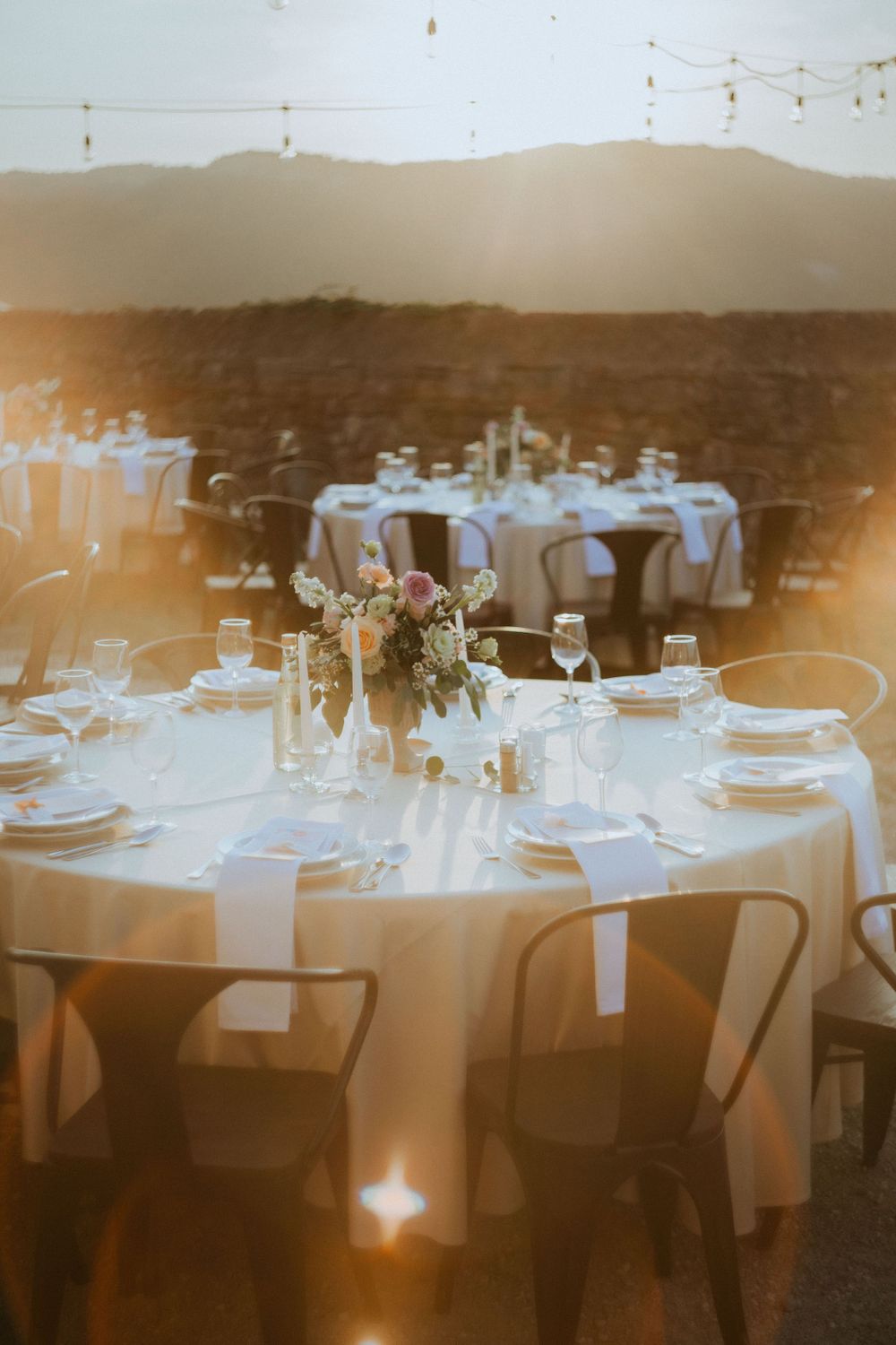 Elegant outdoor wedding reception setup with round tables and white linens at sunset.