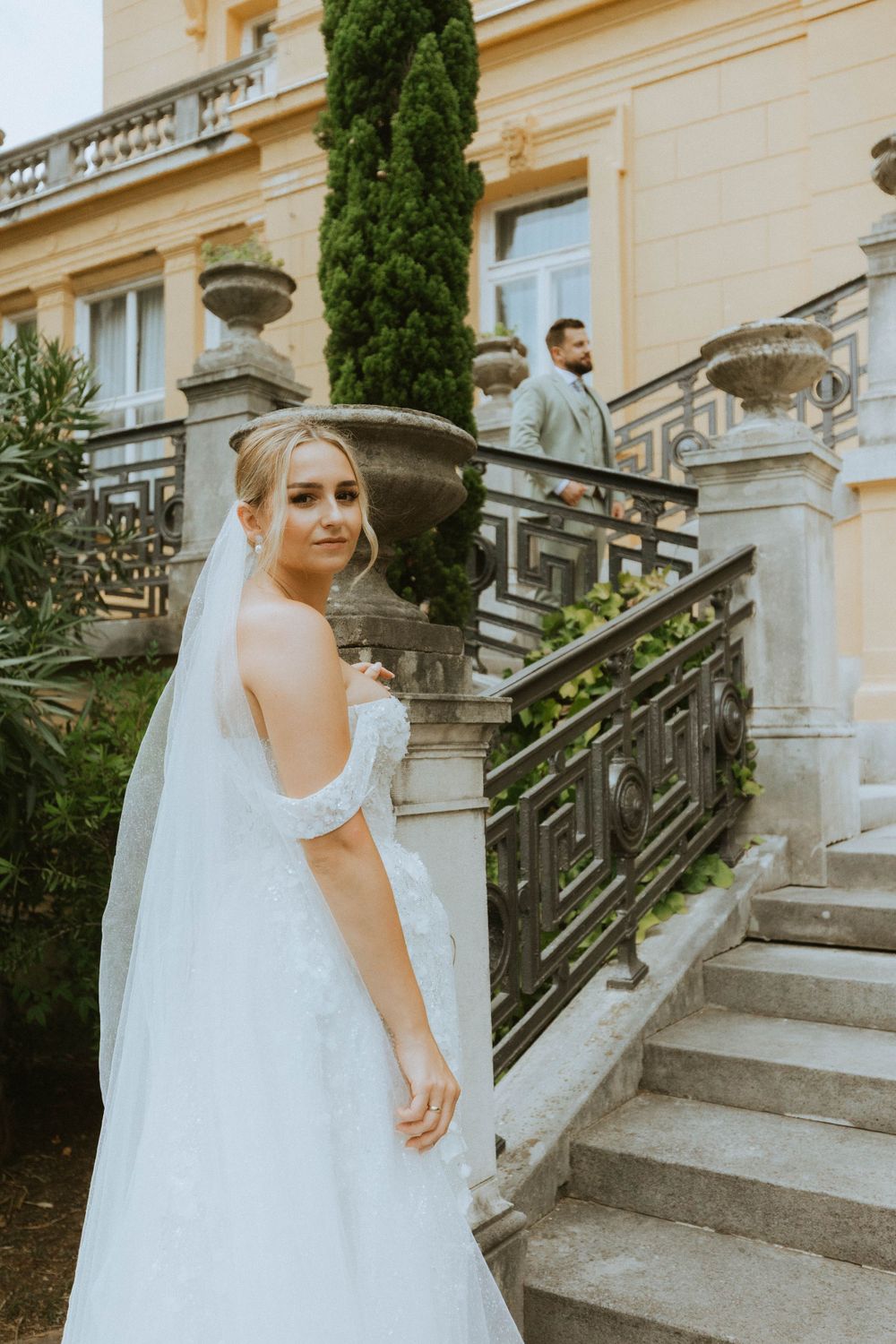 Elegant white wedding gown flowing down grand stone staircase at historic venue.