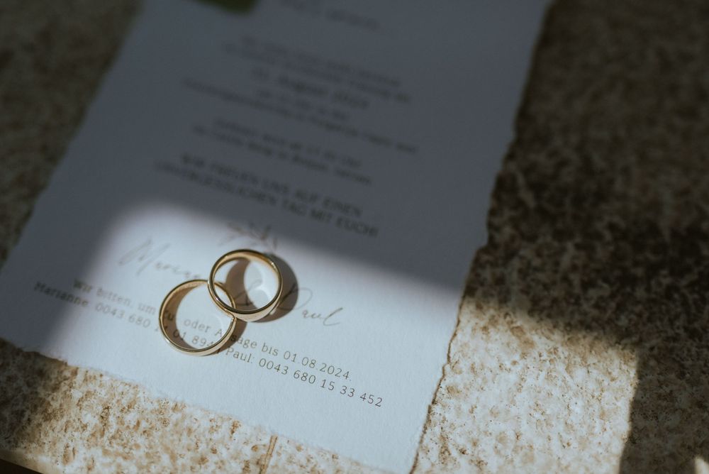 Wedding rings casting shadows on a wedding invitation in natural light.