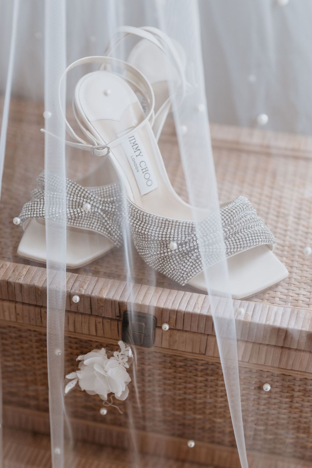 Elegant rhinestone-encrusted white bridal sandals displayed with sheer wedding veil on wooden surface. AT SANT FFRAED HOUSE