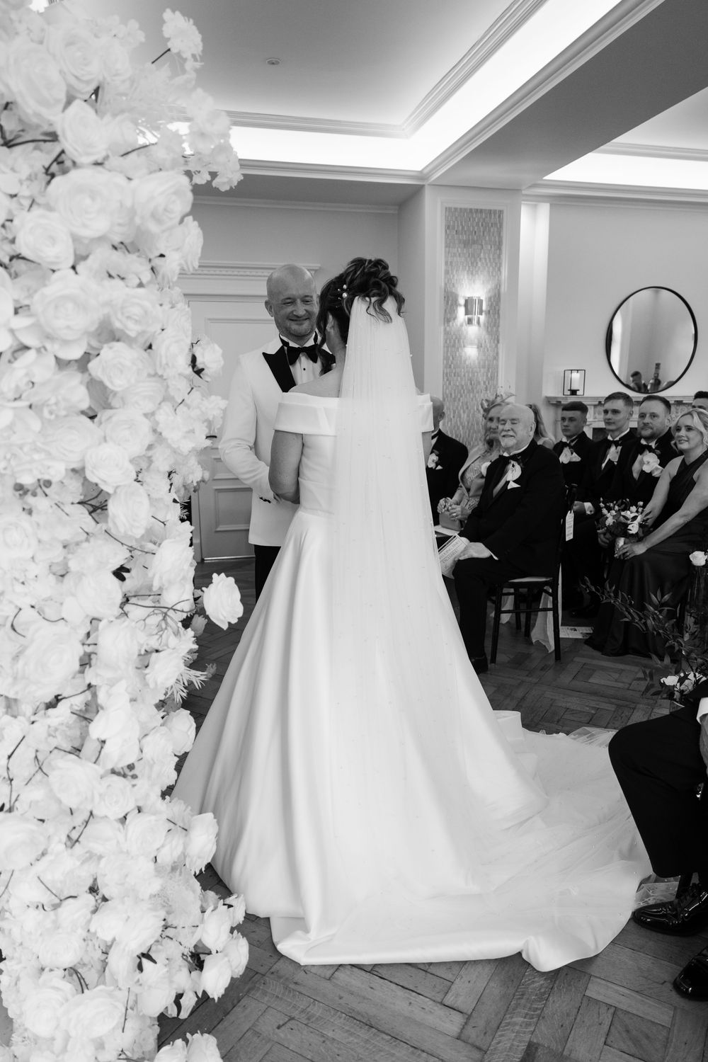 An elegant wedding ceremony with white floral arrangements and a bride in a flowing gown with cathedral veil. AT SANT FFRAED HOUSE