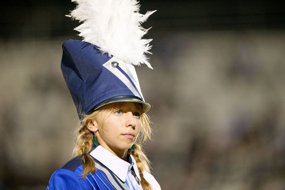 A marching band member in a blue uniform with white feathered hat plume.