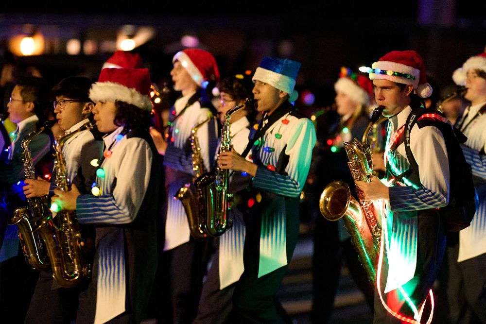 Band members wearing Santa hats perform with saxophones in festive holiday attire during a nighttime performance.