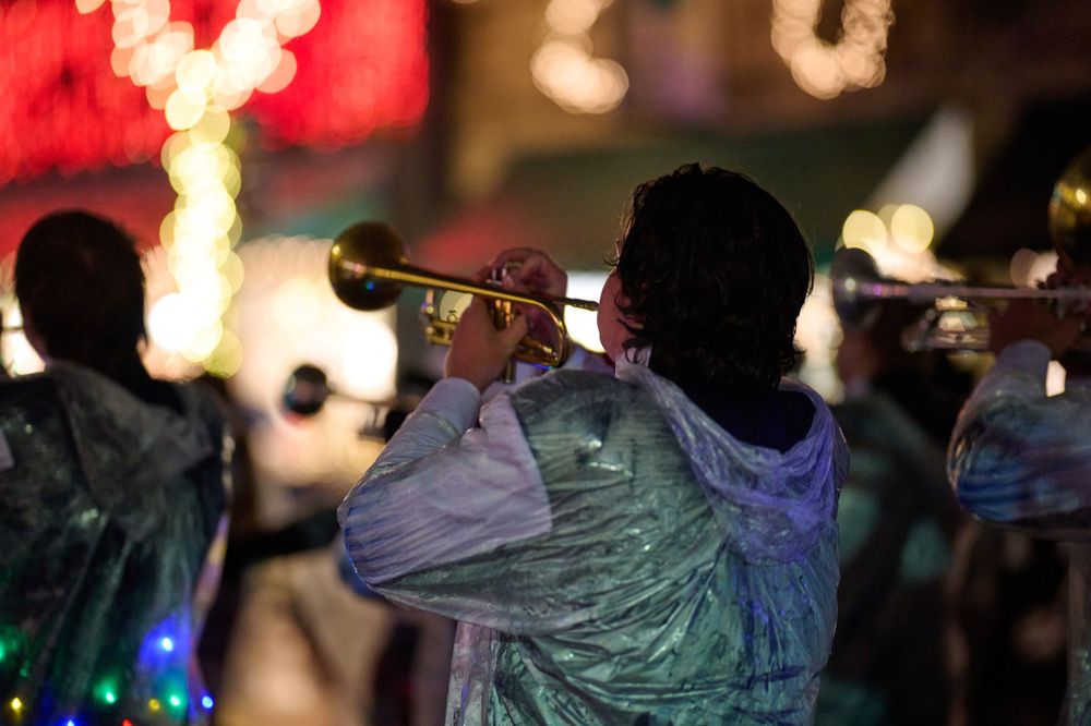 Musicians perform with brass instruments during nighttime holiday celebration with glowing lights.