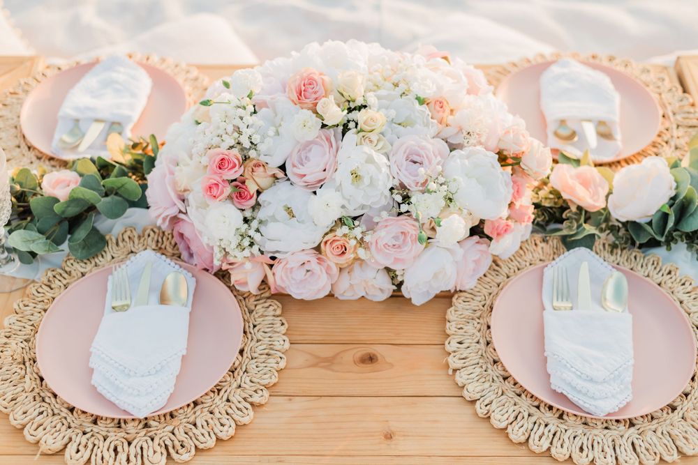 A romantic table setting with pink and white floral centerpiece and decorative woven placemats on a wooden surface.