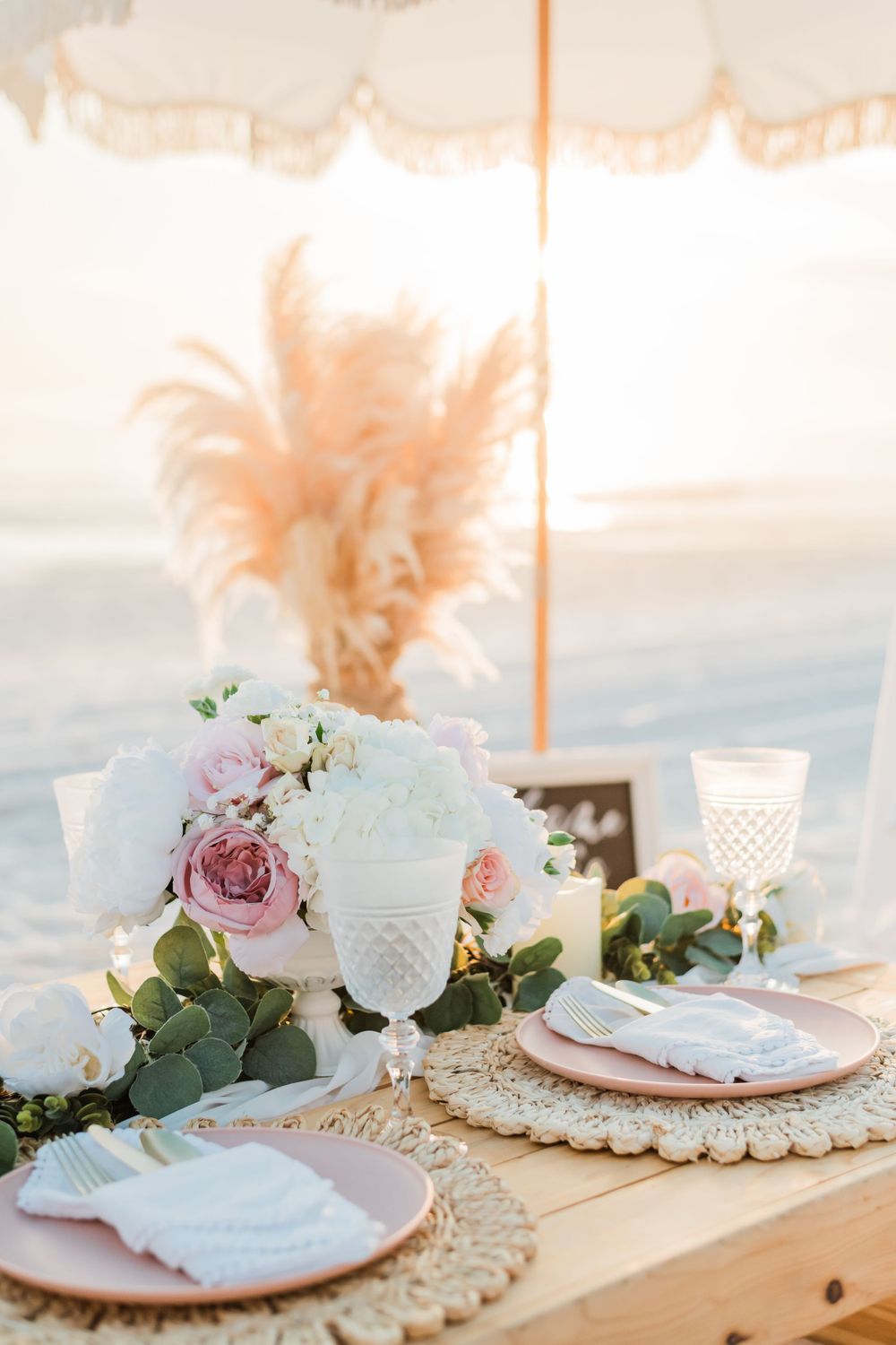 Elegant boho table setting with pink roses, pampas grass, and macrame placemats for a romantic outdoor dinner.