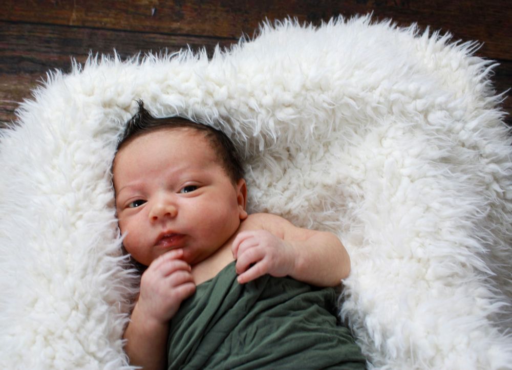 Baby wrapped in green fabric lying on fluffy white rug.