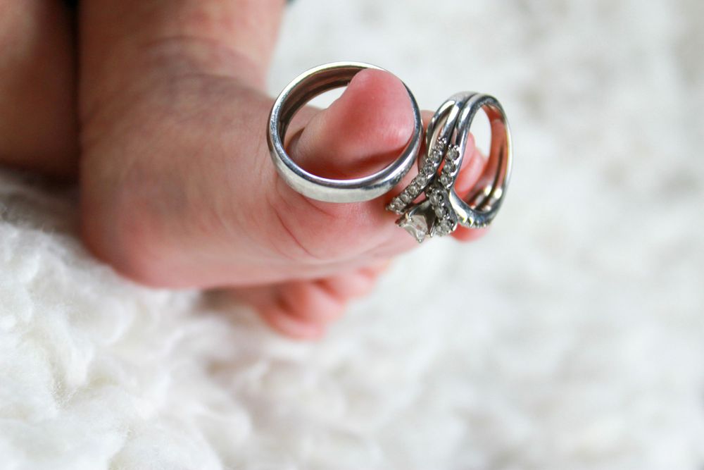 Wedding rings placed next to tiny baby toes on white textured fabric.