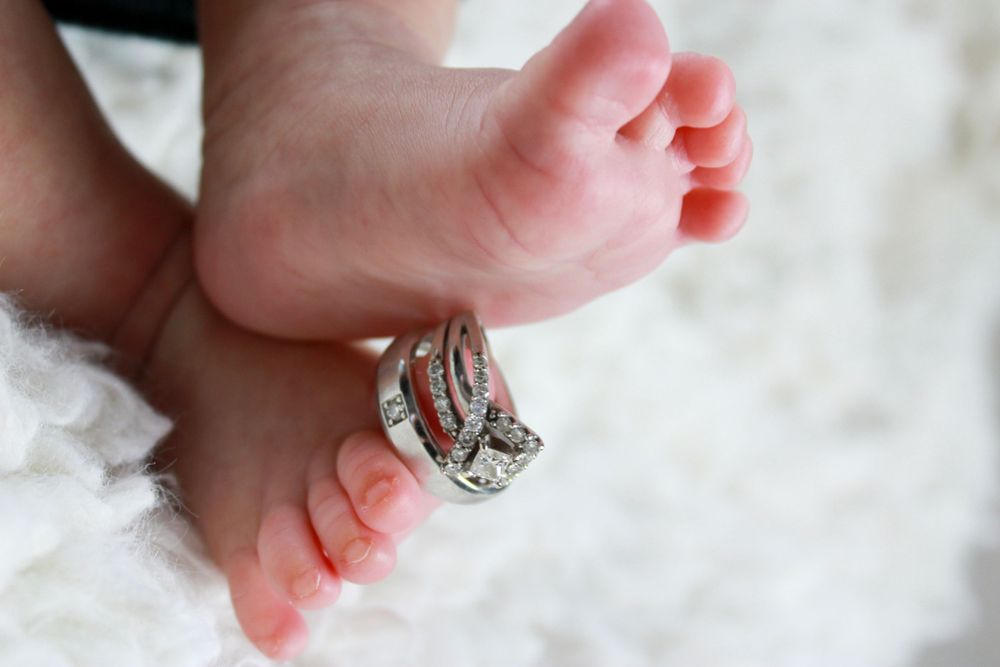 Tiny baby feet resting on wedding rings against a white background.