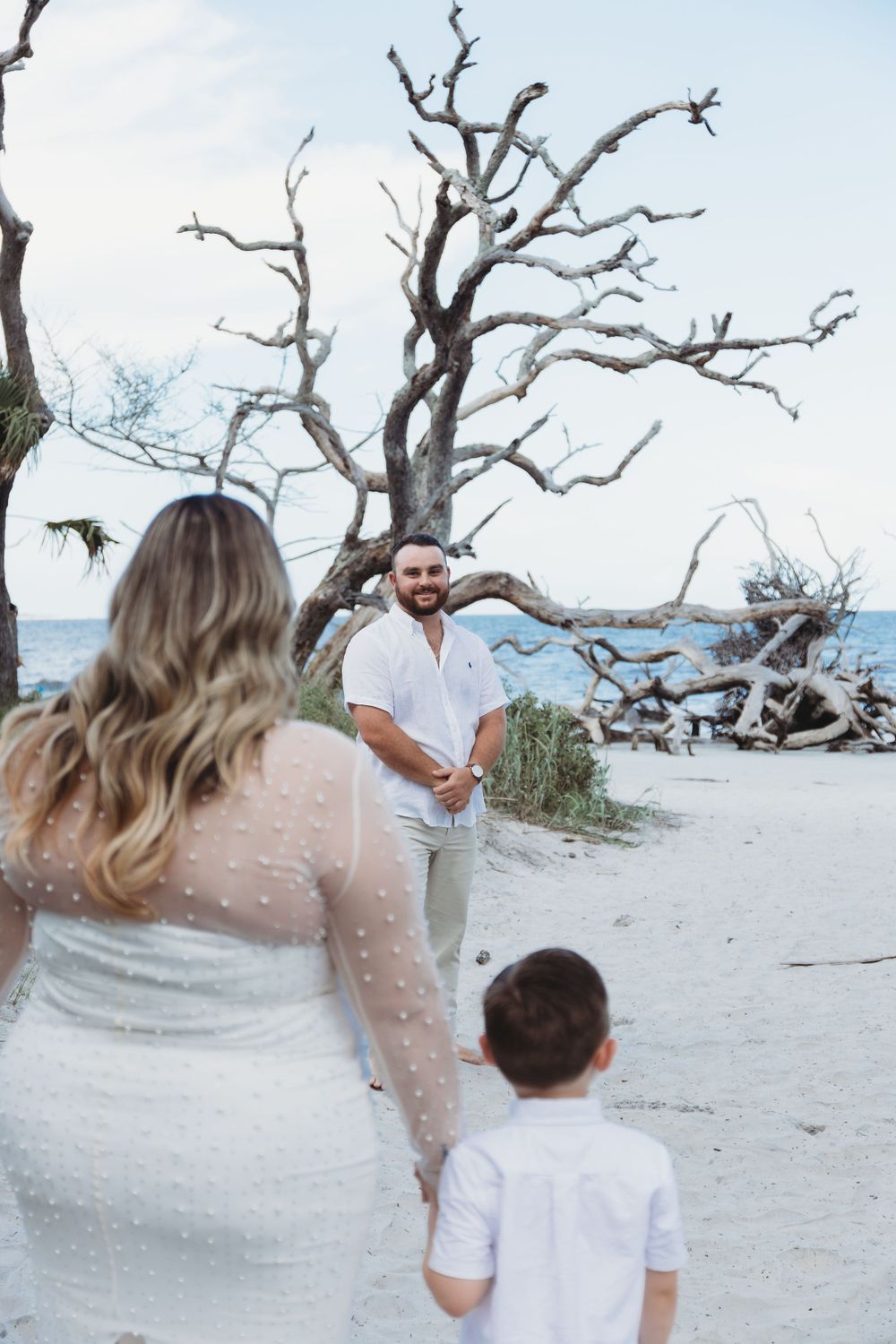 A scenic beach wedding moment with bare trees and ocean waves in the background.