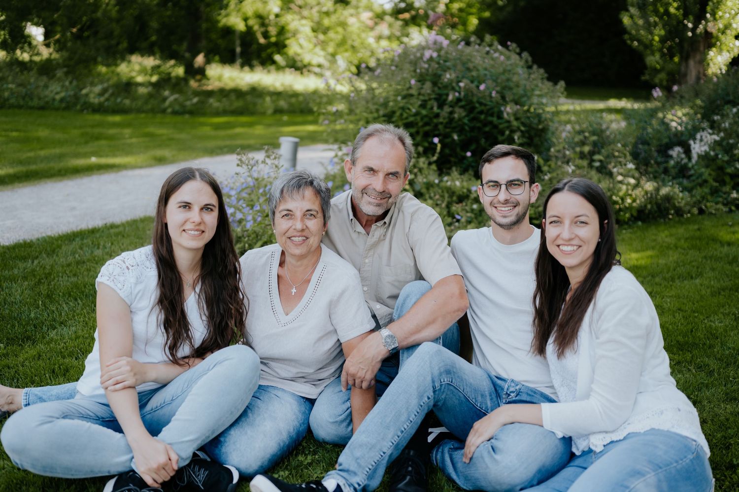 Eine Familie mit mehreren Generationen sitzt gemeinsam auf dem Rasen in einem sonnigen Garten.