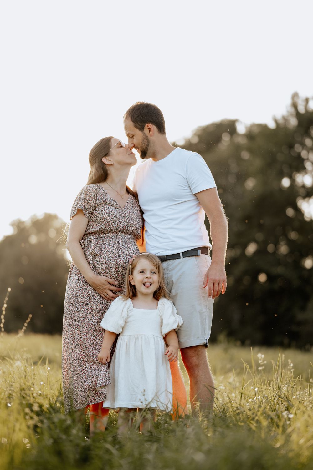Familienbild von Babybauchshooting in der Natur mit sich fast küssendem Paar und Kind in Mengen Jovanna Burkard
