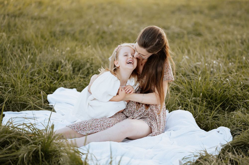 Babybauchshooting und Familienbild von Mama, die mit Kind auf einer Decke in der Wiese kuschelt Mengen Jovanna Burkard