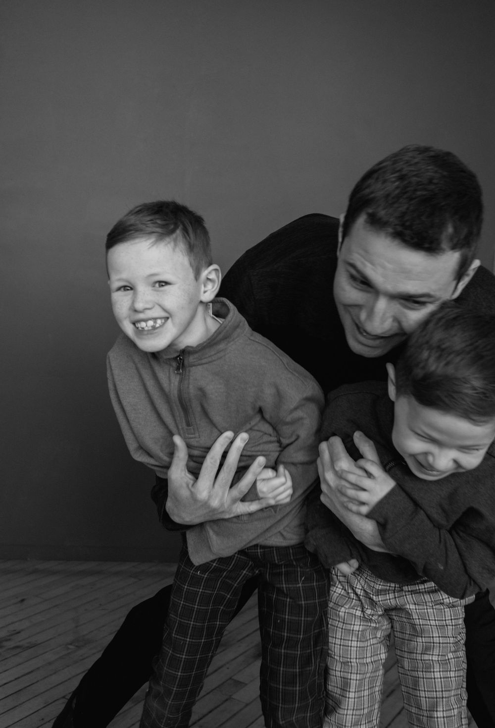 A black and white portrait of playful family interaction with joyful laughter and embraces.