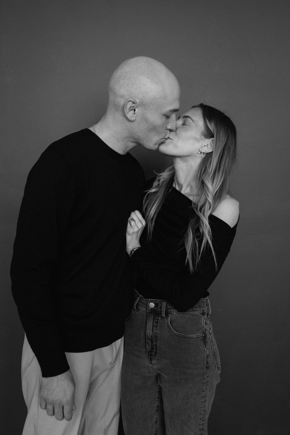 Black and white portrait of a romantic couple sharing an intimate kiss against a simple studio backdrop.