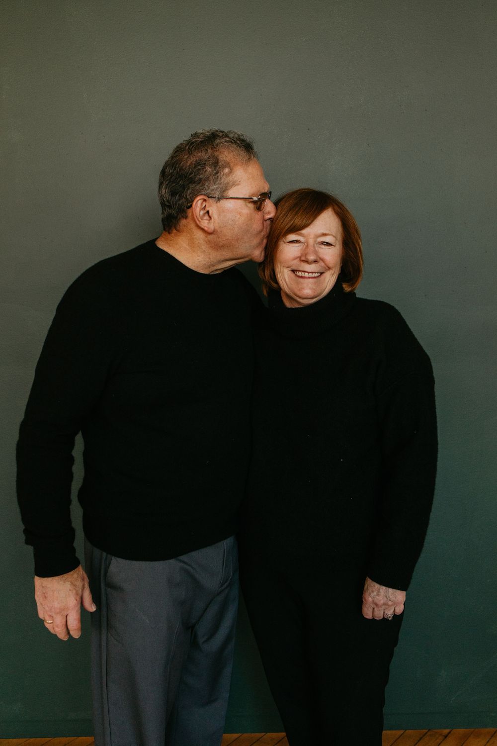 A couple in dark clothing share intimate moments in a series of candid poses against a dark green background.