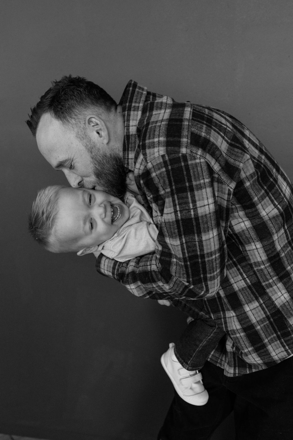 A tender black and white portrait of a parent and child embracing while wearing matching plaid shirts.