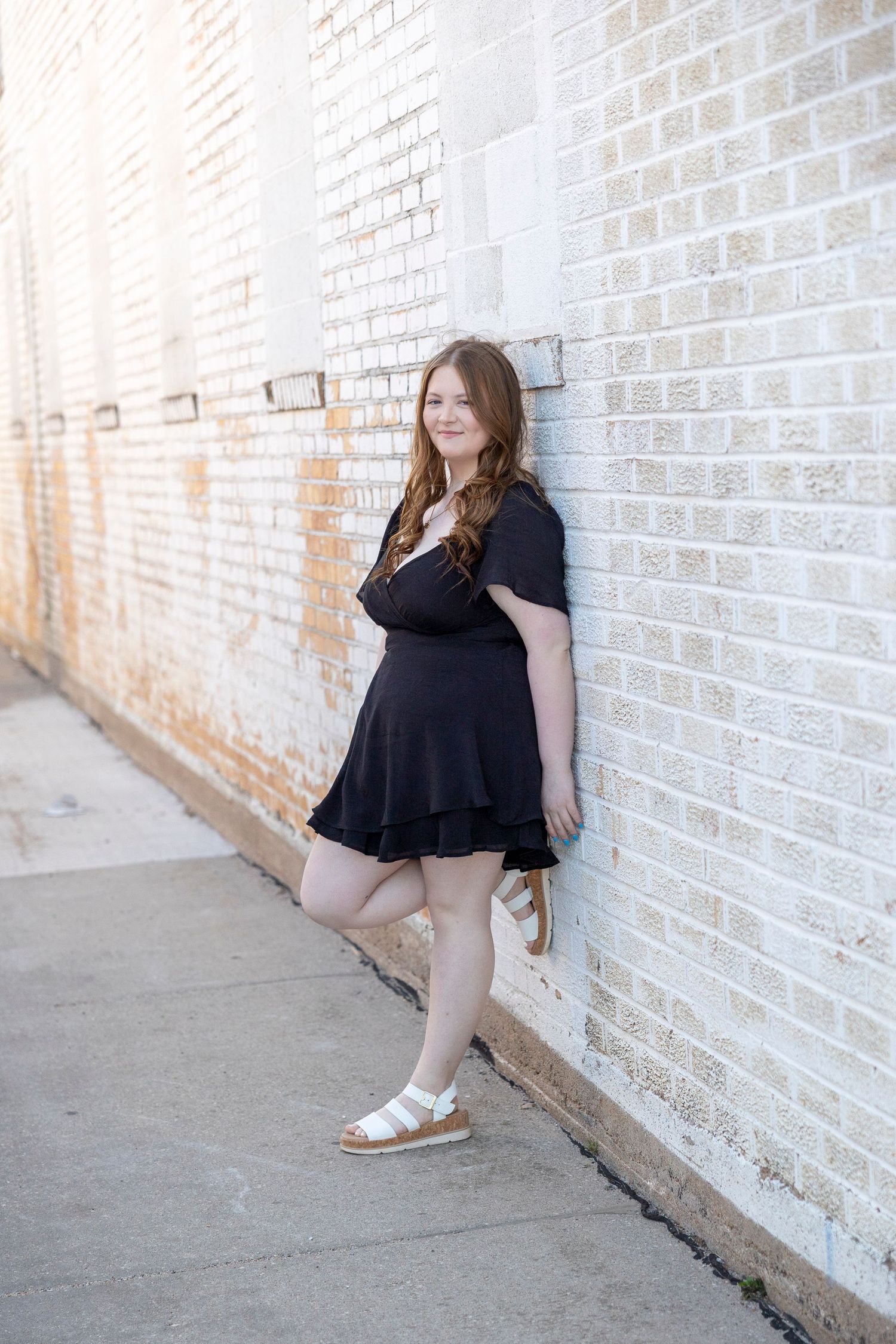 Person in black dress poses against brick wall in series of casual outdoor portrait shots.