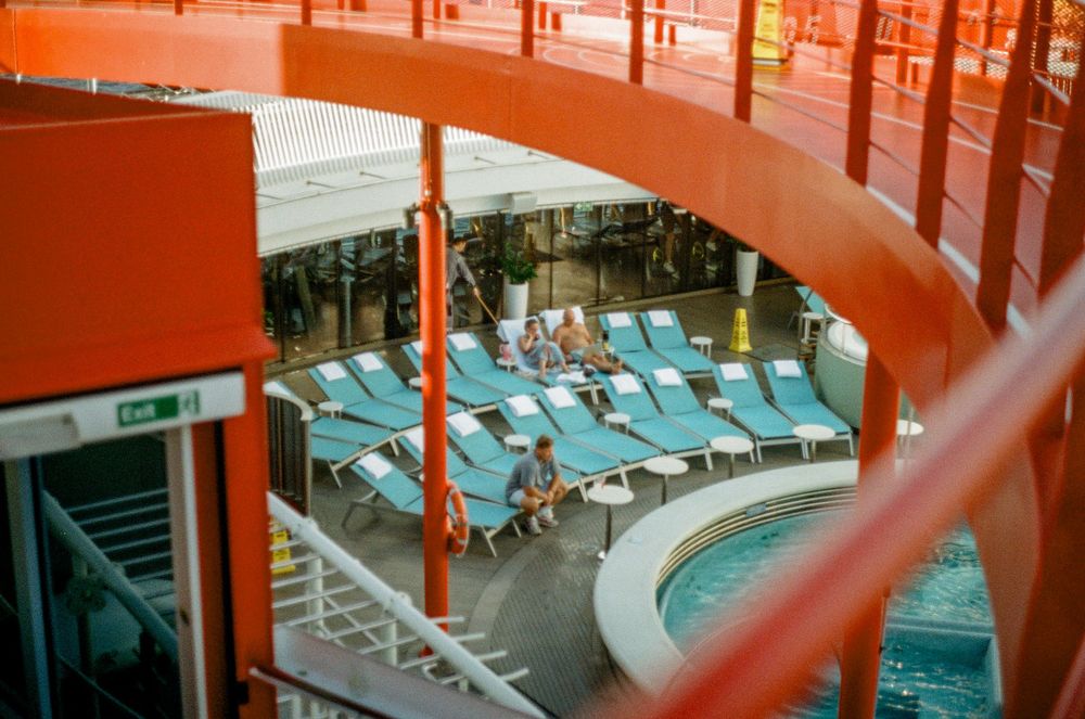 View of cruise ship pool deck with blue lounge chairs through curved orange architectural elements.