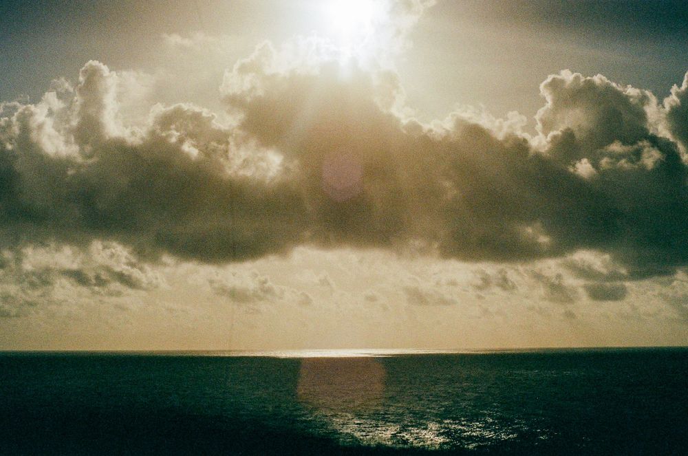 Dramatic sunset over ocean with sunburst through clouds casting golden light on water.