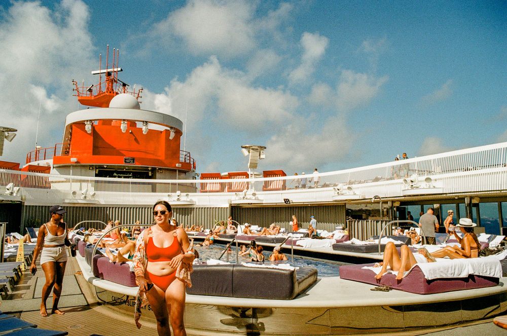 Orange and white cruise ship deck with passengers lounging in the bright sun.