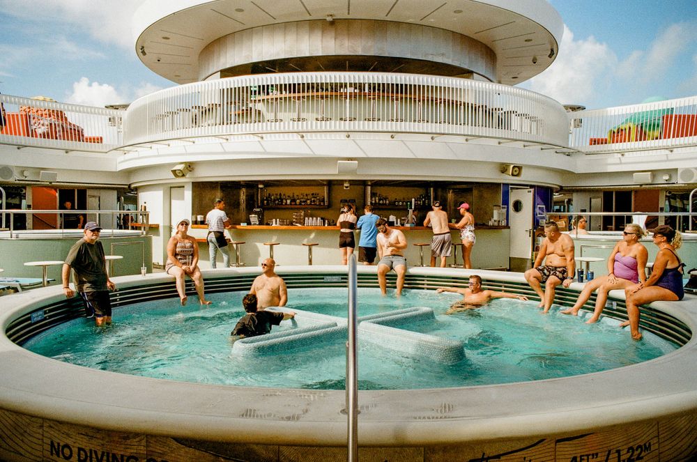 Circular pool deck on a cruise ship filled with swimmers enjoying the water.