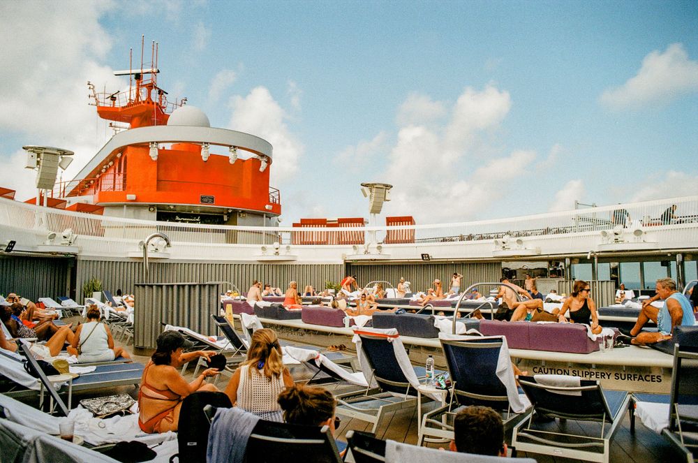 Retro-style cruise ship deck with orange superstructure and rows of lounge chairs in sunlight.