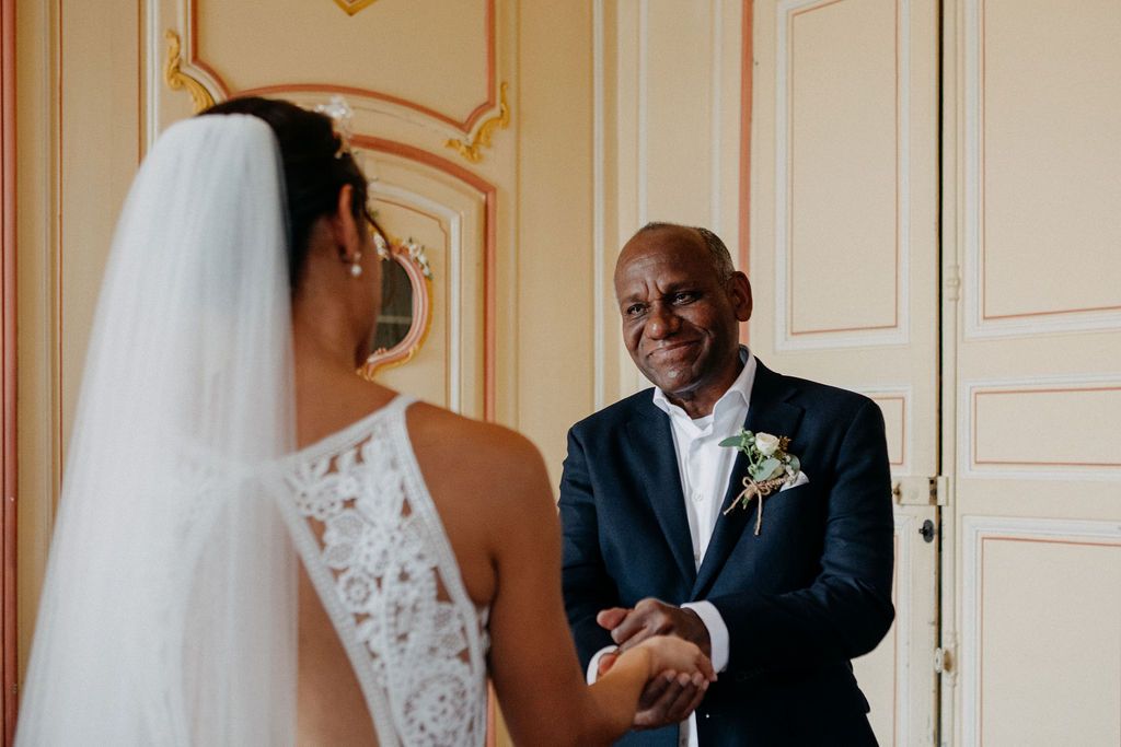 Emotional father-daughter first look moment with groom smiling and holding bride's hands before wedding.