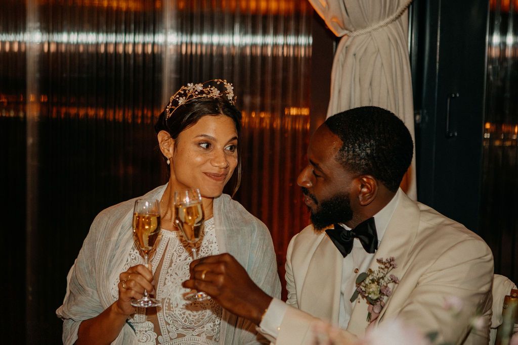 Bride and groom toasting with champagne glasses at their wedding reception in warm candlelit setting.