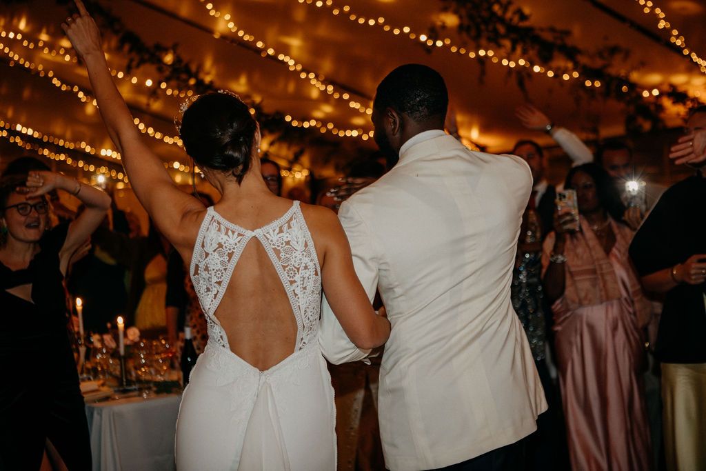Bride in backless lace gown and groom dancing together surrounded by celebrating wedding guests.