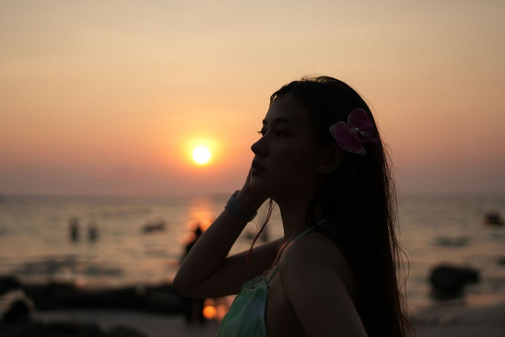 Silhouetted person stands on beach during golden sunset with boats dotting the ocean horizon.