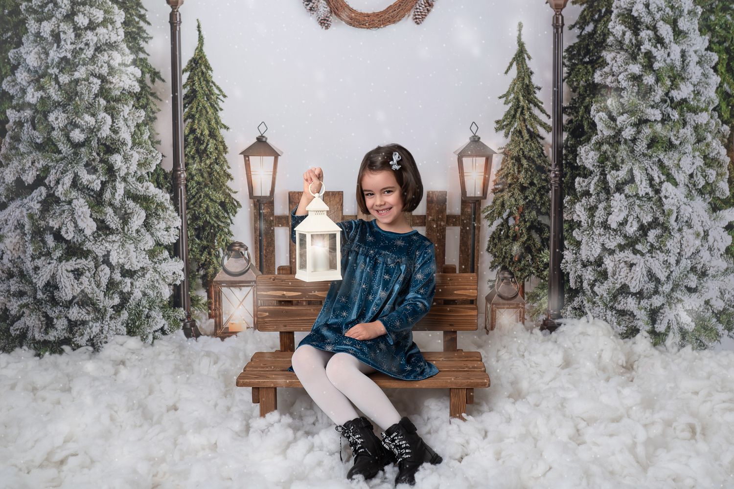 Winter holiday photo session with rustic bench, lanterns and snowy evergreen decor in studio setting.