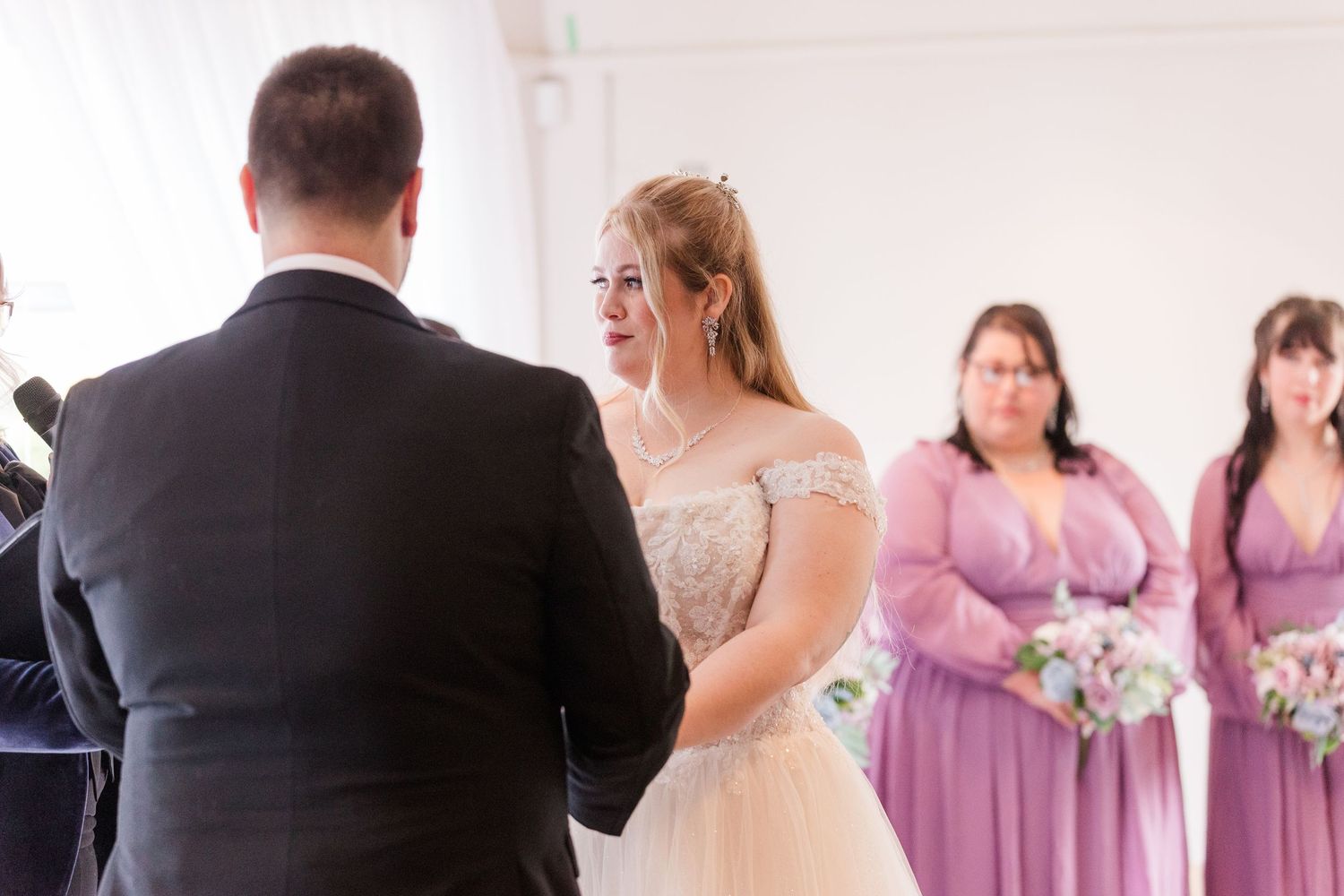 Wedding party in purple bridesmaid dresses and black suits gather for formal photos at elegant venue.