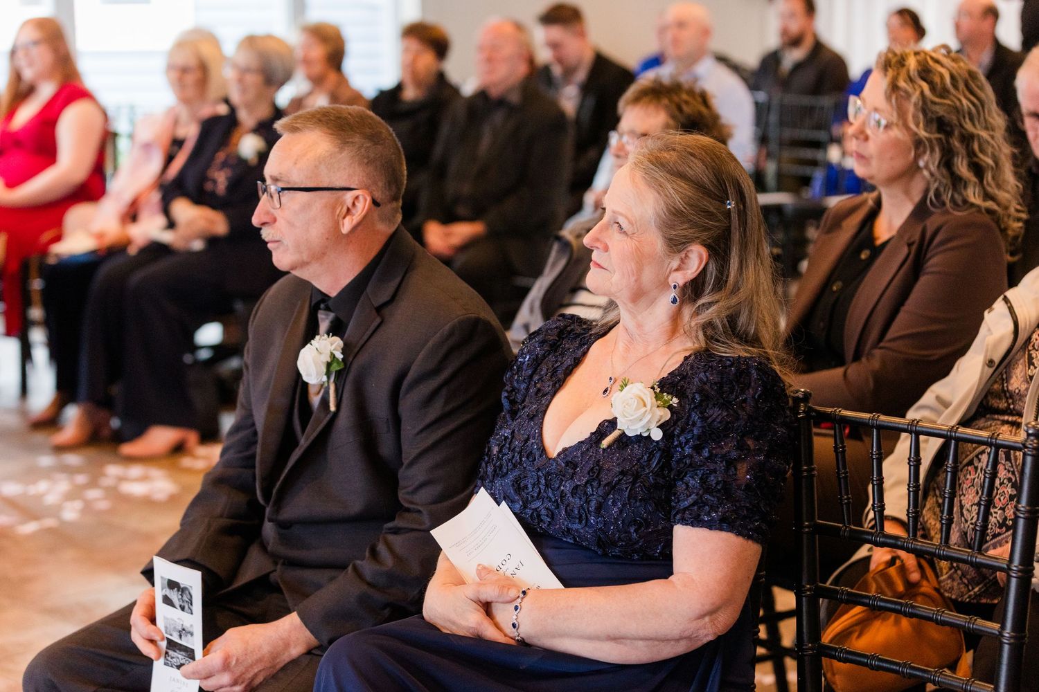 Wedding guests seated in rows during an indoor ceremony, watching attentively.
