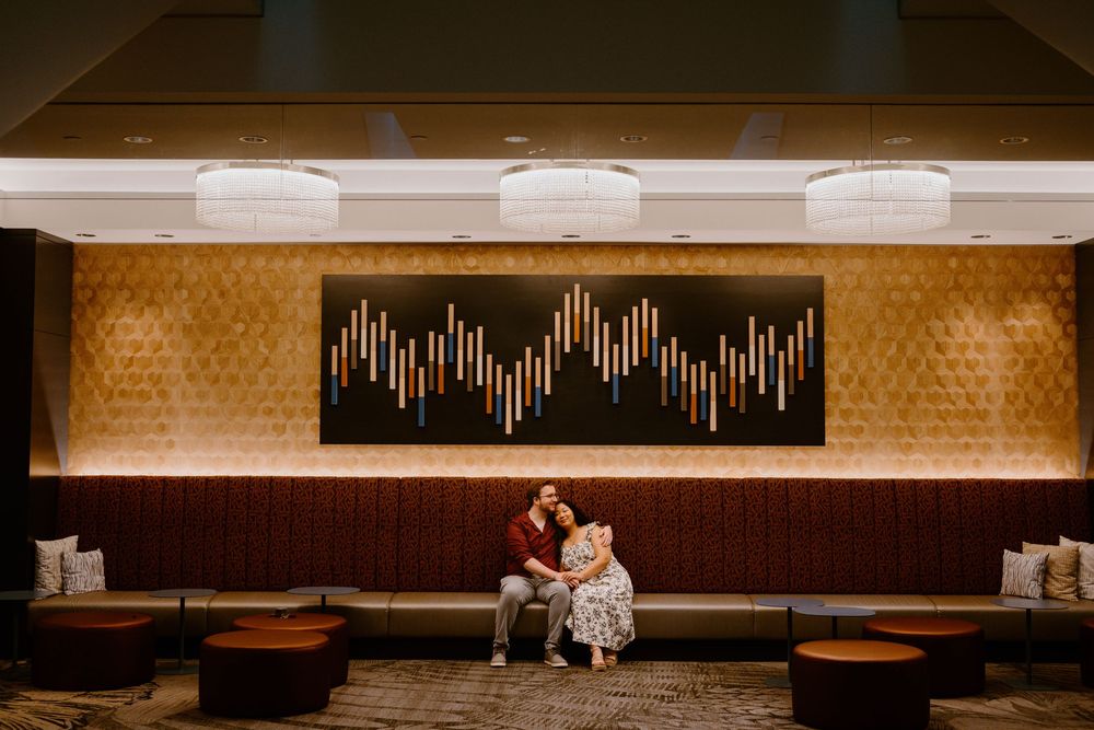 Two people share an intimate moment on a bench beneath modern wall art in a warmly lit restaurant interior.