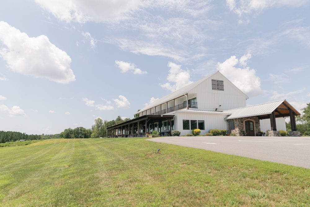 Rolling green hills and modern white buildings create a scenic rural wedding venue landscape.