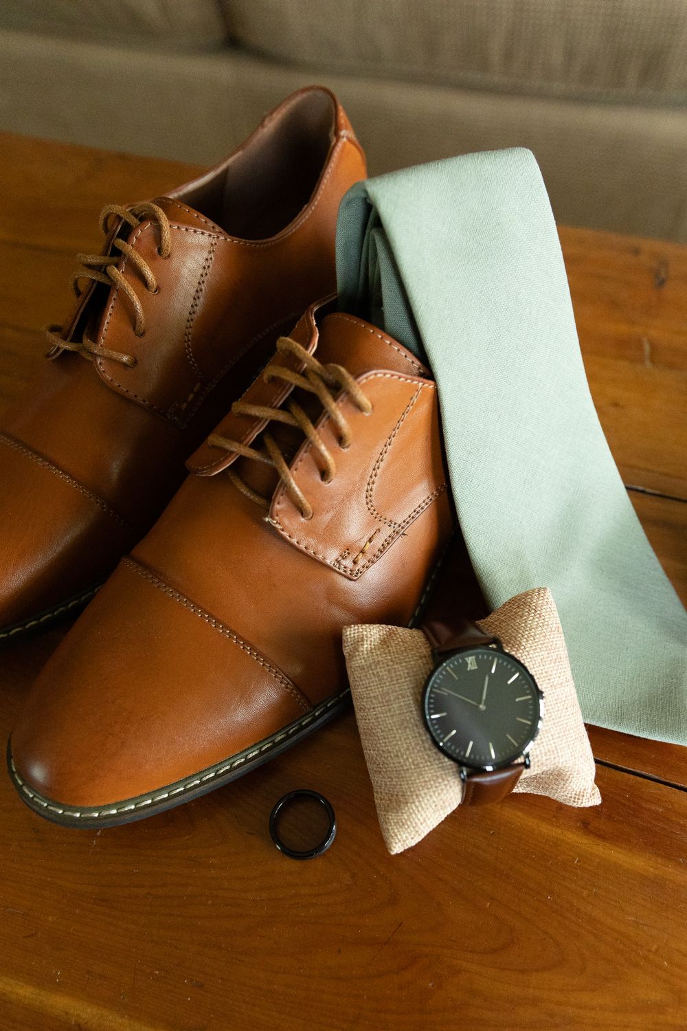 Groom's brown leather shoes with mint tie and watch on wooden surface.
