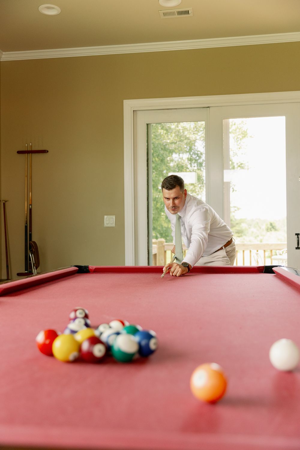 Playing pool on a red felt table in a bright room with large windows.