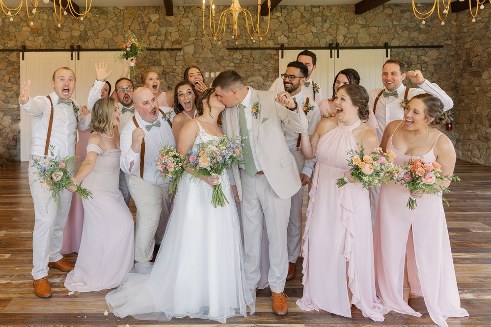 Wedding party in pink and light gray attire posing together in rustic venue.