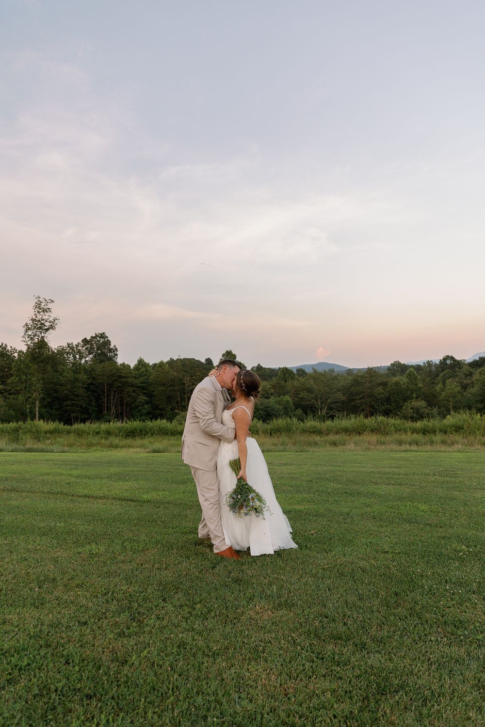Romantic sunset portrait of newlyweds embracing in an open field.