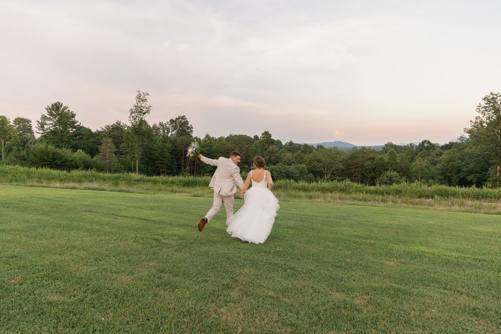 Newlyweds dancing and twirling in a green meadow at dusk.