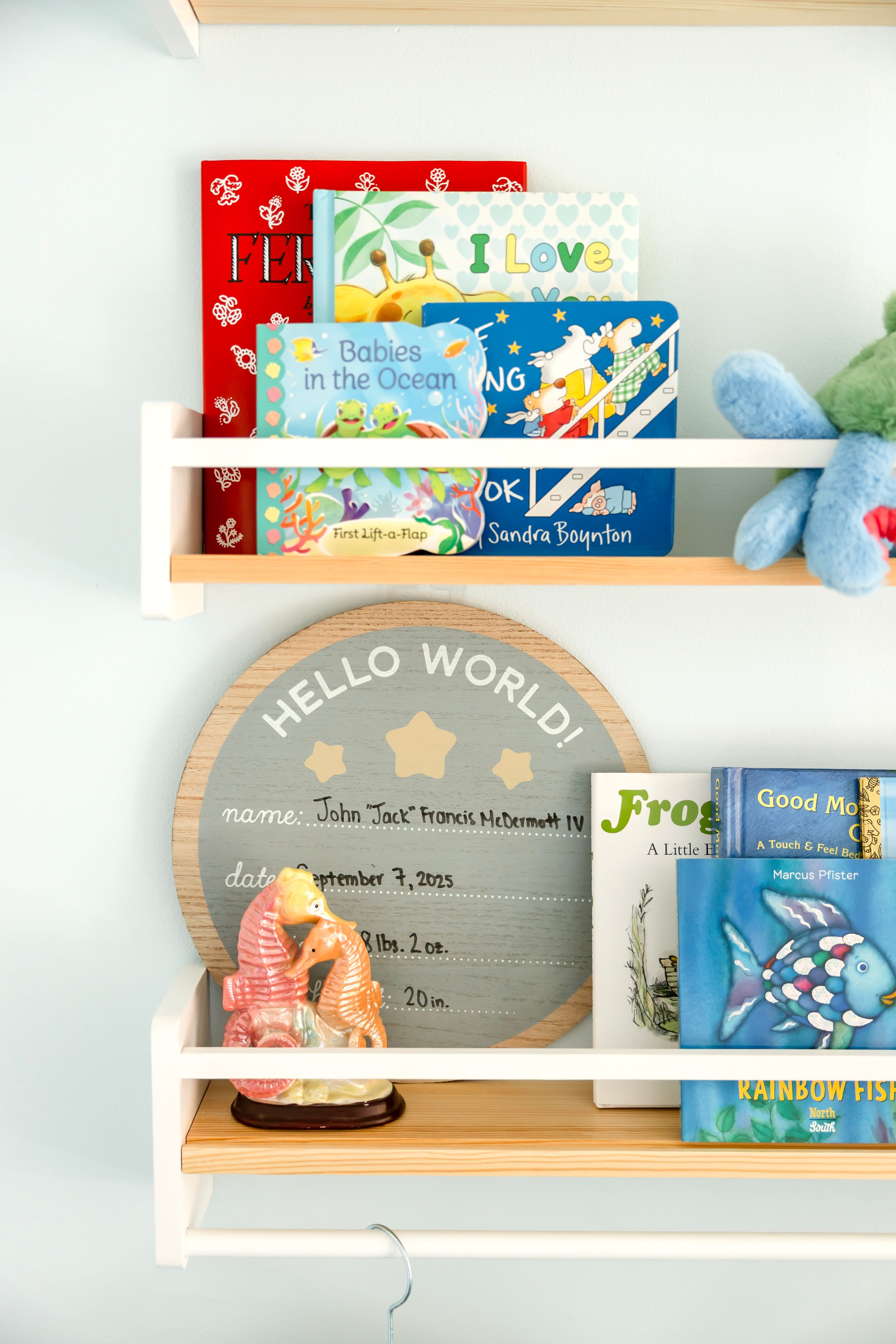Children's books arranged on floating wooden shelves with a 'Hello World' sign and colorful decor.