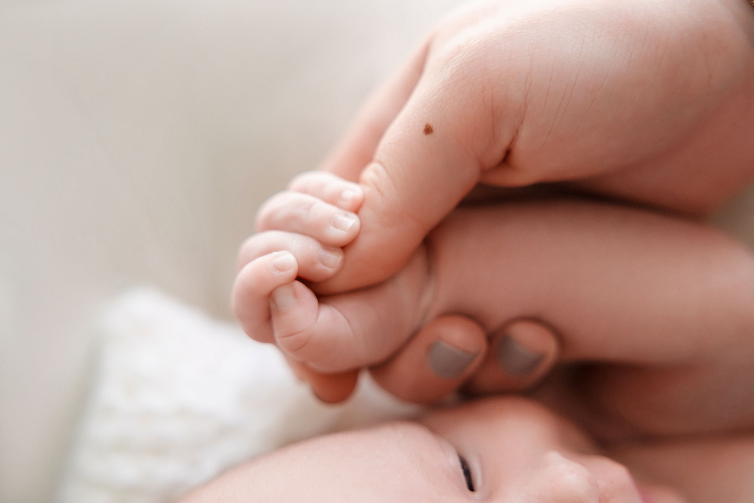 A hand gently holds a sleeping newborn baby swaddled in white blankets.