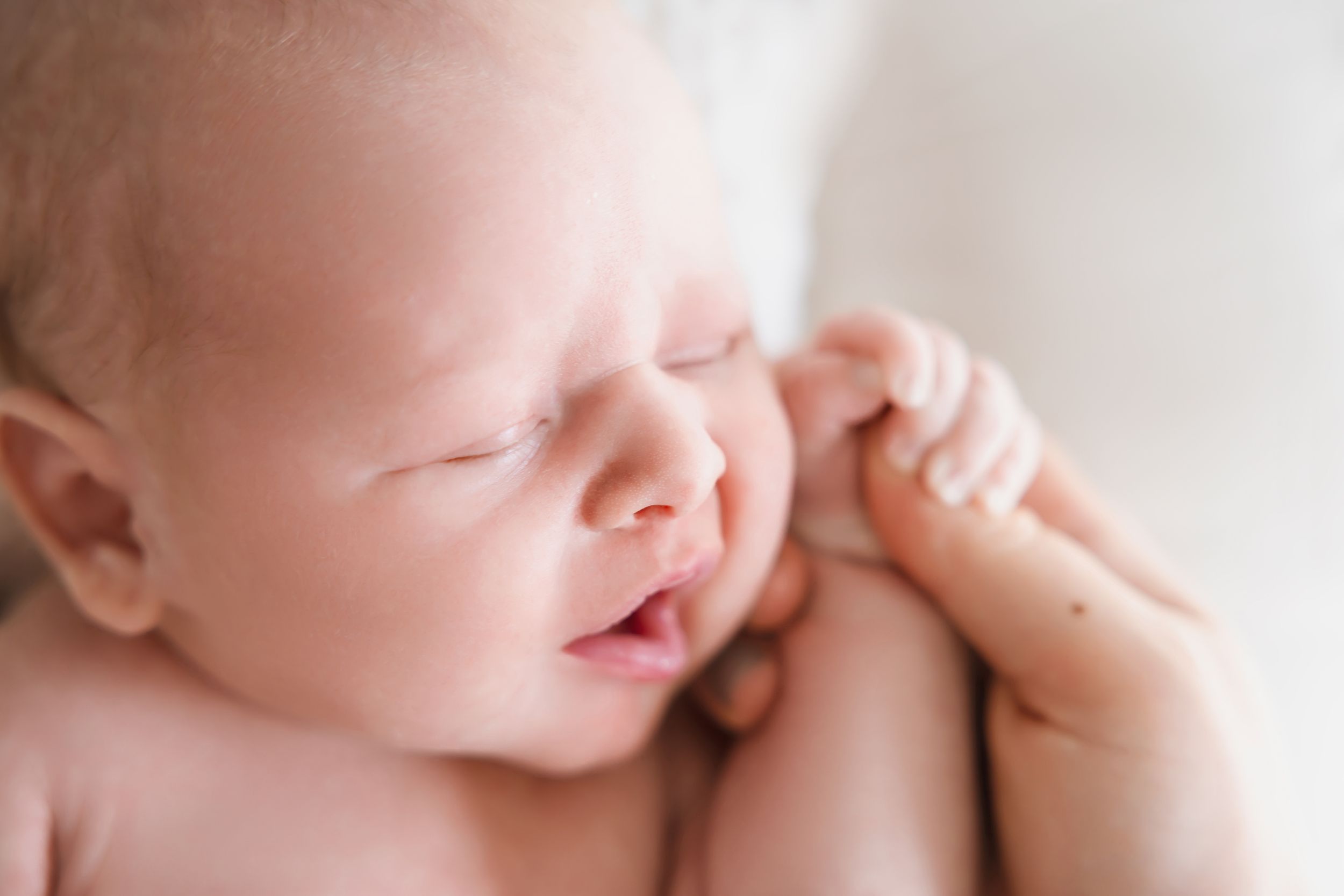 Close up detail of a sleeping newborn baby's delicate features and soft skin in natural light.