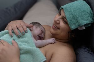 A newborn baby rests skin-to-skin on a parent's chest in a medical setting.