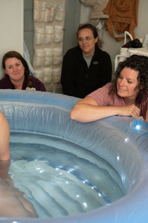 Several people gather around a light blue inflatable birthing pool filled with water.
