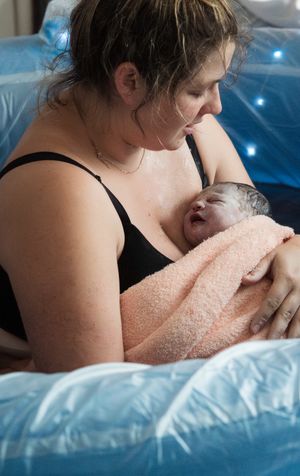A newborn baby wrapped in a pink towel being held during skin-to-skin contact after birth.