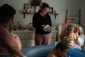 A midwife consults with people during a home birth in a dimly lit room with a birthing pool.