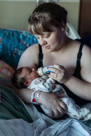 A tender feeding moment as a baby receives a bottle while being cradled in a cozy bedroom setting.