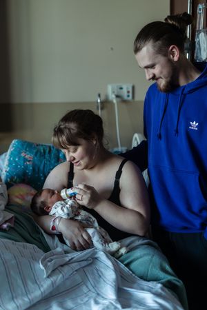 An intimate hospital scene shows a newborn being held while medical care is administered.
